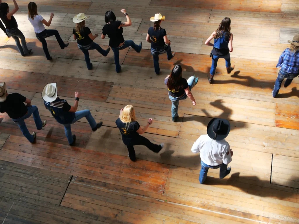 Line dancers in cowboy hats and boots on a wooden dance floor